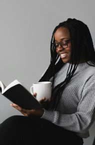 Una ragazza sorride mentre legge un libro tenendo una tazza